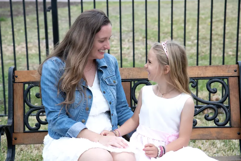 A mother and daughter share a joyful moment on a park bench outdoors.